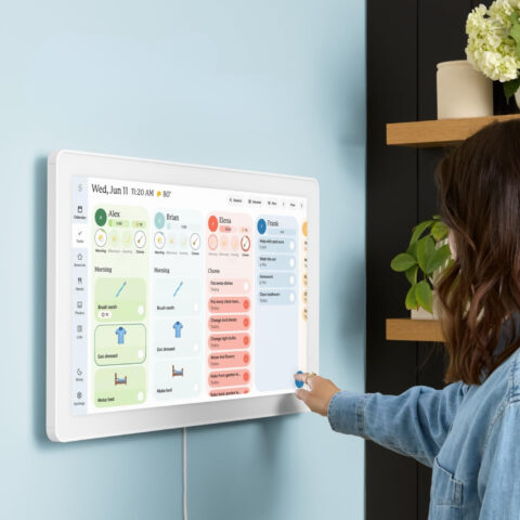 Touchscreen Smart Calendar: The Stylish Upgrade Your Family Actually Needs Woman using a wall-mounted touchscreen smart calendar to manage family schedules, chores, and reminders in a modern home.